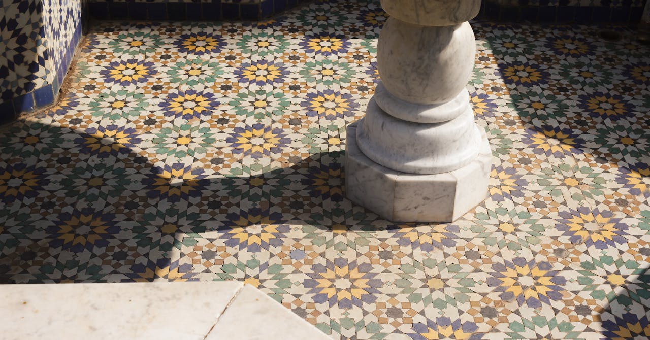 Intricate Moroccan tiles and marble column in natural light, showcasing vibrant patterns.